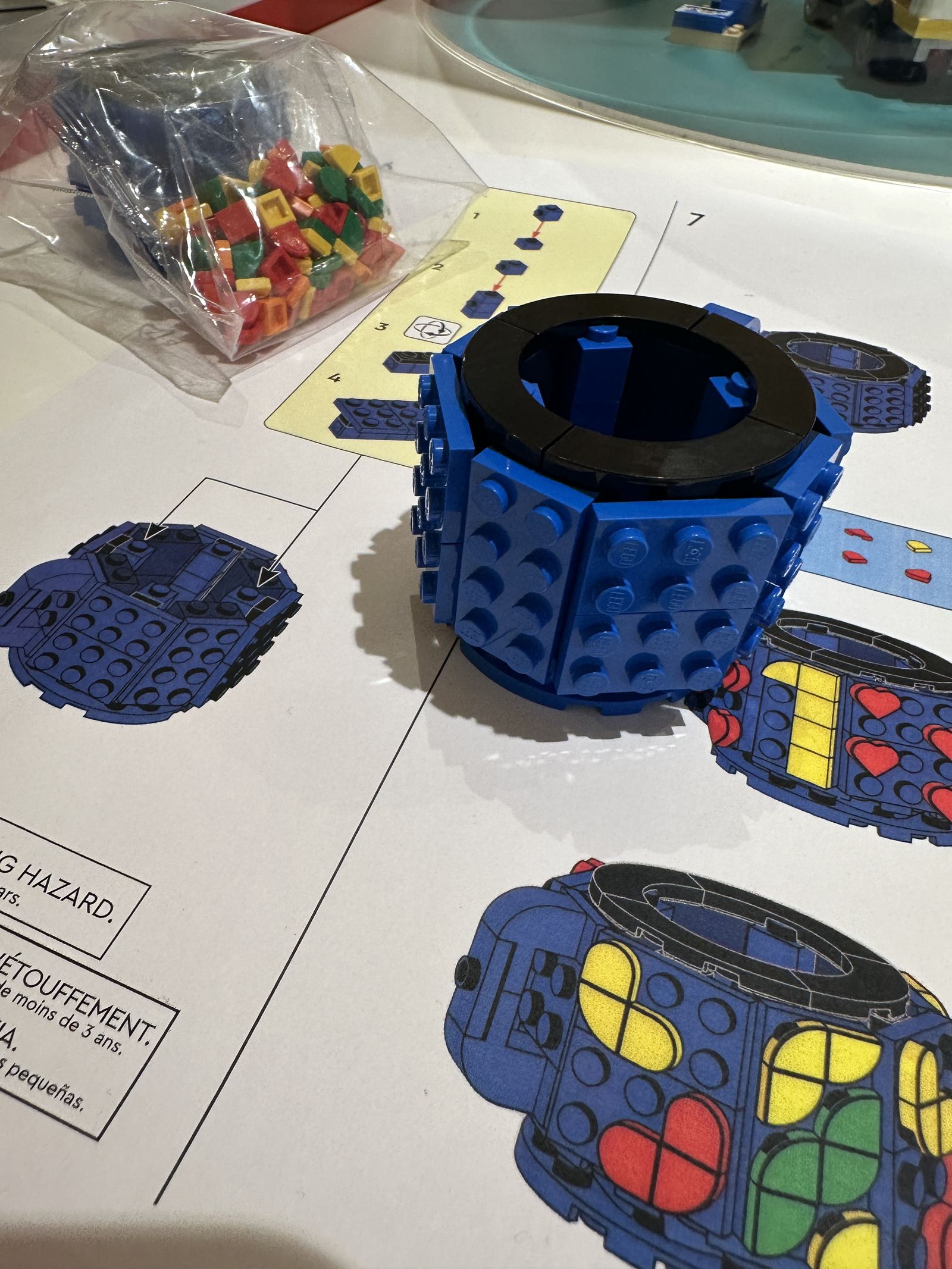 Base de la taza de café LEGO® montada, junto a la bolsa de piezas de colores